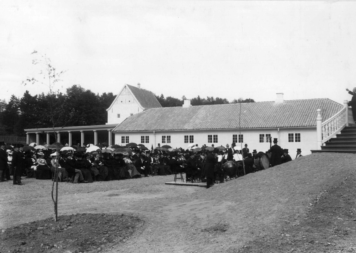 Narve Skarpmoen, Direktør Hans Aall åpner Den kulturhistoriske utstillingen i 1901. Publikum og musikkanter lytter til Aall, som står på trappen og taler.
