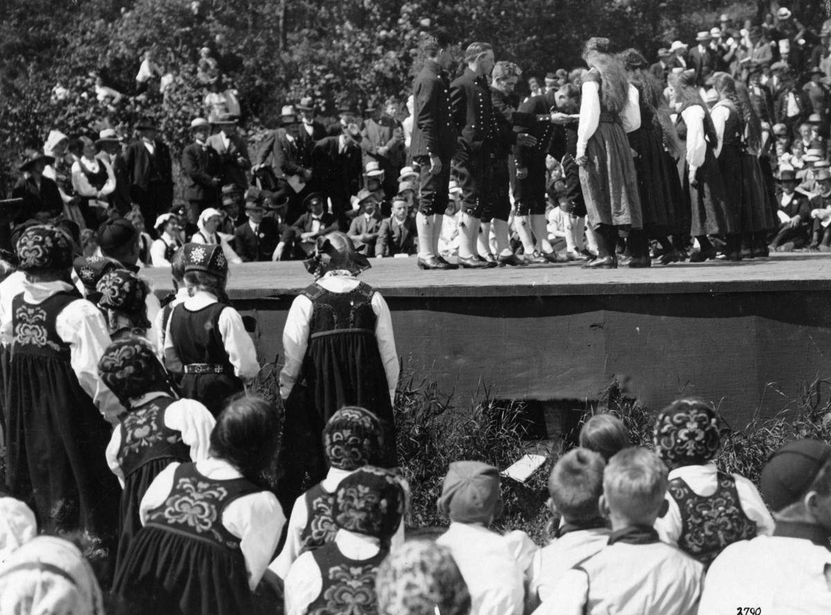 Hermann Christian Neupert, Folkedans. Oppvisning på en scene. Publikum. Mange kvinner i bunad.