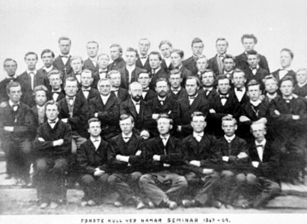 Anno Domkirkeodden, Gruppe, skoleklasse, første kull, Hamar Lærerhøgskole. De fem lærerne for kullet sitter i midten: J. M. Hansen (med hvit kravatt), Oluf Saxe, Nils Hertzberg, Jens Jenssen og Lars Andersen. Eleven ytterst til høyre er Gudbrand Andersen Skjæset som ble lærer i Vang. Se En innlandsby vokser fram bilde…