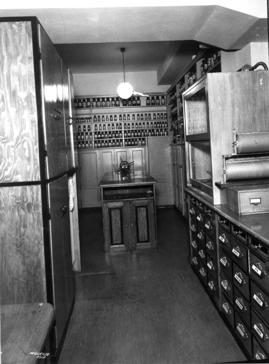 Hermann Christian Neupert, Rådhusapoteket, Oslo. 1935-1937. Interiør. Hyller med flasker. Disk med skuffer.