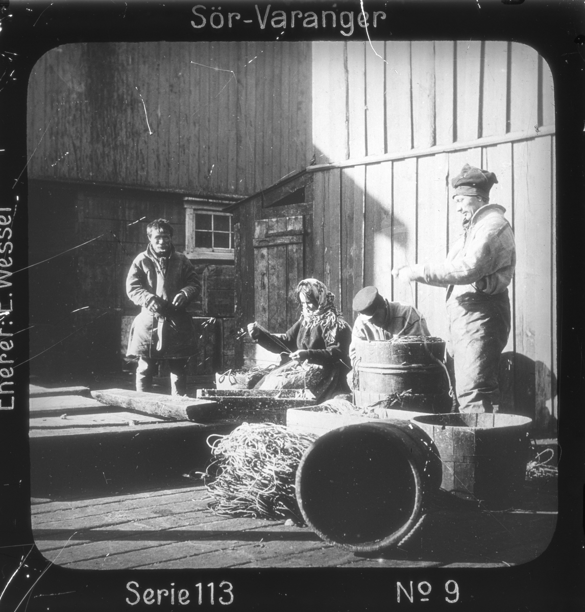 Ellisif Rannveig Wessel, Samiske fiskere setter agn på liner i fiskeværet Kiberg, Vardø, Finnmark. Linestamper i forgrunnen. Motivet har nr. i lysbildeforedraget kalt "I lappernes land - Sør-Varanger", utgitt i Nerliens Lysbilledserier, serie nr 113.