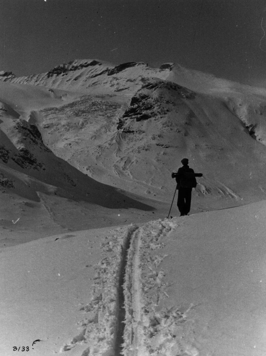 Anders Beer Wilse, Skiløpere ved Galdhøpiggen fra Heilstu i Jotunheimen med snødekte fjell og sol.