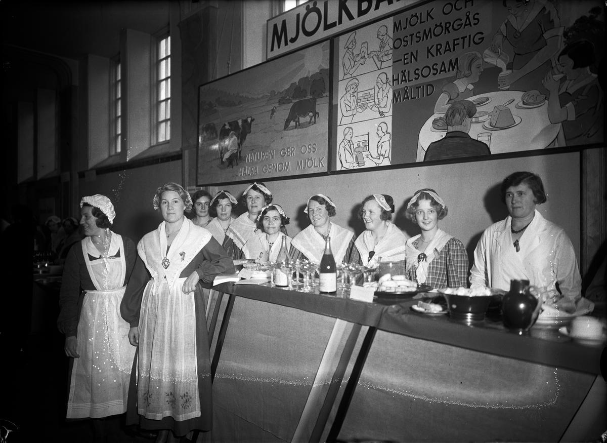 Paul Sandberg, "Propagandabaren" på livsmedelsmässa arrangerad av Hushållningssällskapet och Upsala läns husmodersförbund, sannolikt på Norrlands nation, Västra Ågatan. Till höger framför disken hemkonsulent Rut Ingeborg Jonsson, gift Högstedt