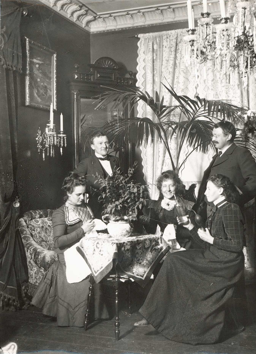 Axel Quinsgaard Wiborg, Persongruppe, Meltzers gate 9, Oslo ca. 1890. Interiør med personer omkring bord, to kvinner broderer. Axel Q. Wiborg står selv til høyre. Fra serie tatt av iseksportør Axel Quinsgaard Wiborg (d. 1944).