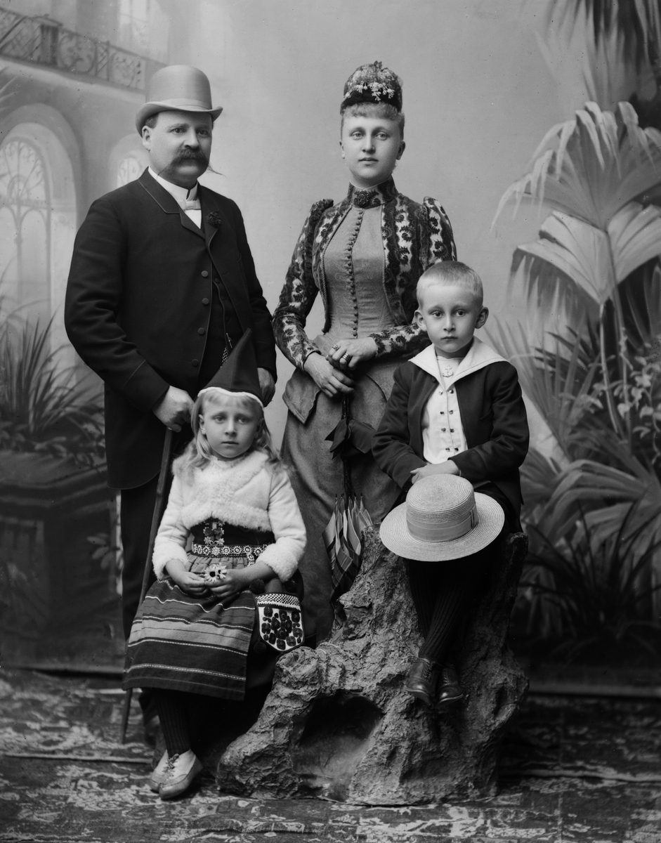 Maria Tesch, Porträttfotografi föreställande Axel Peterzén, handlande, fru Hilma född Gylling, dottern Anna gift Ljunggren, son okänt namn . Porträtt. Familj. Man. Kvinna. Ateljéfotografi. Fotograferad i Maria Teschs ateljé som fanns i Linköping åren 1873 - 1936. Digitaliserad efter original glasnegativ som för…