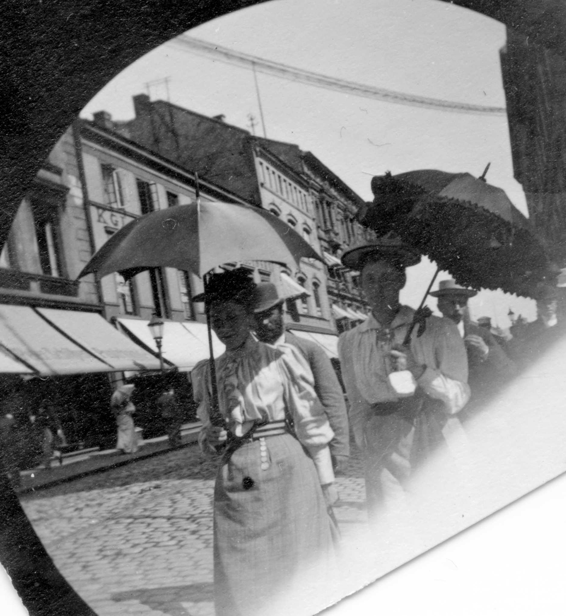 Fredrik Carl Mülertz Størmer, To kvinner med parasoll i bygate, Karl Johans gate, Oslo. Bygårder og butikker bak.