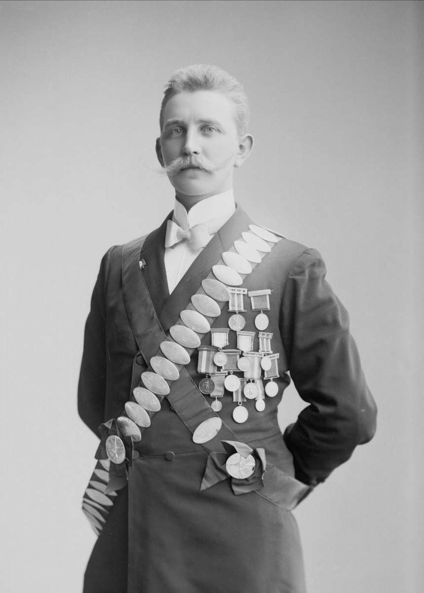 Gustav Borgen, Portrett, mann med bånd med premieplaketter, skyting. Kongebeltene til Skydeselskapet Skarpskytten. Carl Chr Engelstad.