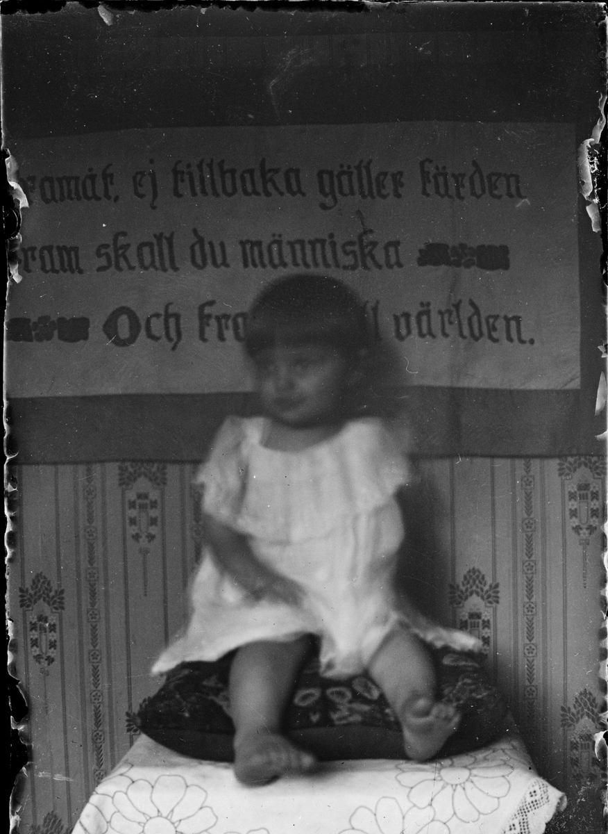 Skötsner-Edhlund, Ett barn sitter på en kudde med en broderad bonad bakom sig, Östhammar, Uppland