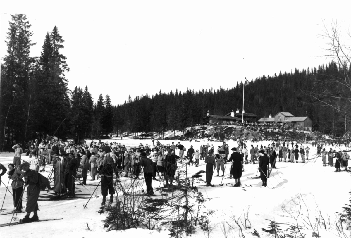 Hermann Christian Neupert, Slalåmrenn, Tryvannsåsen, Oslo. 1934. Skiløpere på Tryvann. Tryvannstua med flagget til topps ses i bakgrunnen.