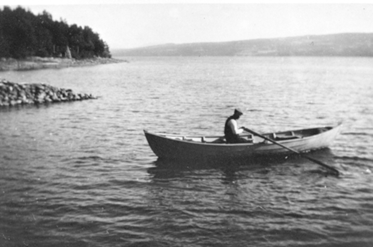 Anno Domkirkeodden, Mann i robåt utenfor brygga ved Smedstua nedre, Nes, Hedmark. Enten Even eller Arne Lie.