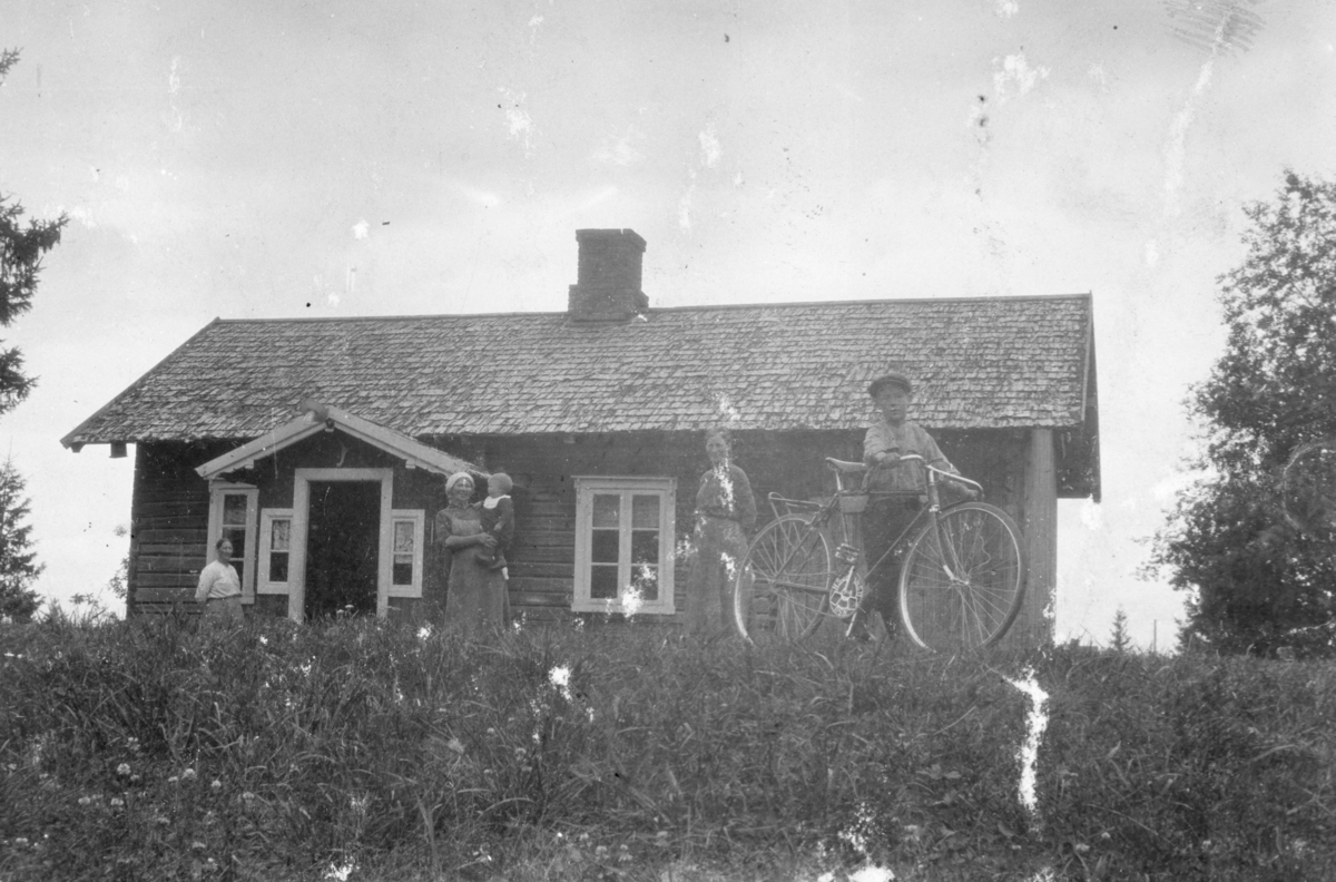 Ukjent, Olstad av Øvre Tomter(60/22). Det originale stua i Olstad. Pauline t.v. og Martha med Reidar på armen. Johan på sykkel foran. Ca 1916.