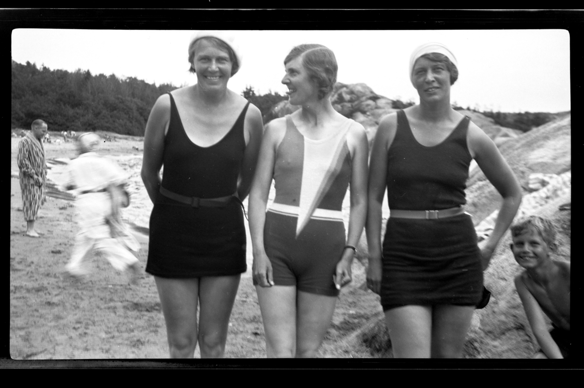 Rolf Sr. Sundt, Tre søstre i badedrakt på stranden på Ula i Vestfold. Fra venstre Betsy Hansen, Hilda Sundt og Lillly Moestue. Rolf Sundt Jr. titter frem fra høyre. Fotografert 1932.