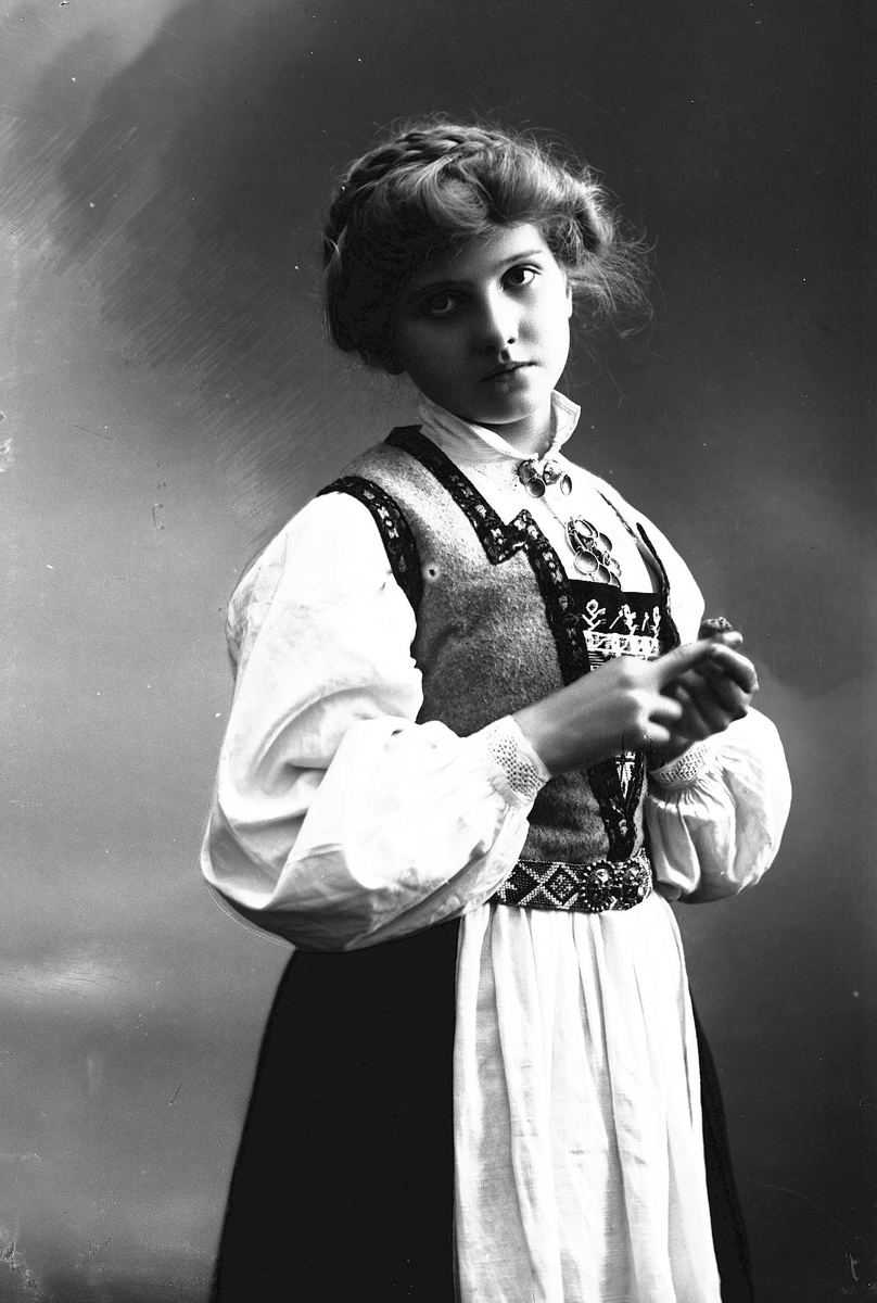 Solveig Lund, 3/4 dels studioportrett av kvinne i drakt, med oppsatt hår. Hun tar på seg en ring. Bakgrunnen er nøytral.