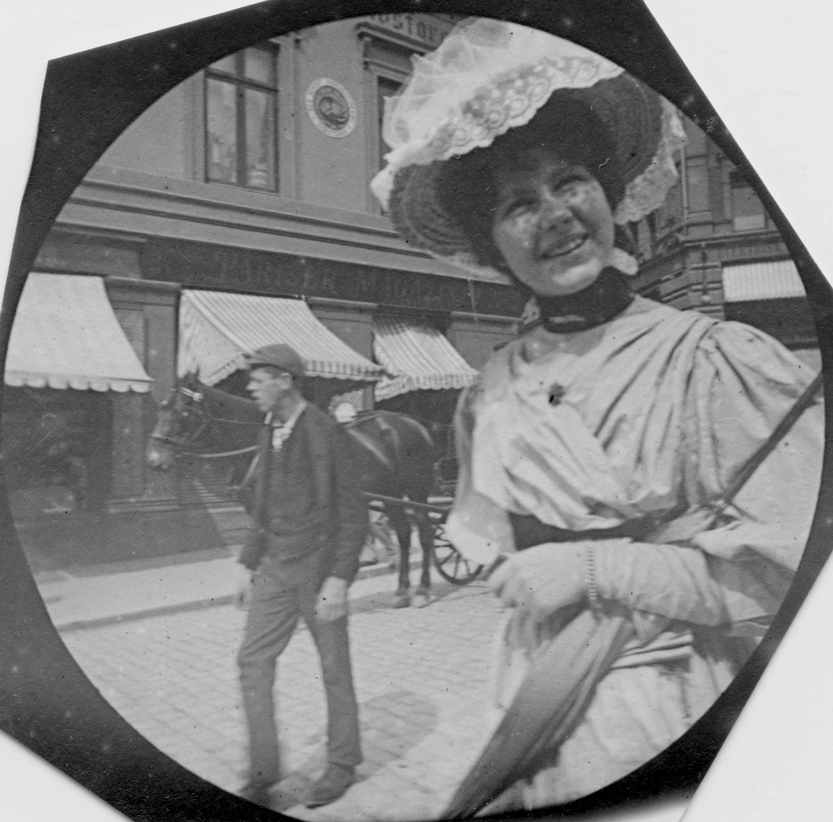 Fredrik Carl Mülertz Størmer, Frk Jotta Pedersen, senere fru Holter, spaserer langs bygate, forretningsgård og hest på andre siden av gata. Ant. Karl Johans gate, Oslo.