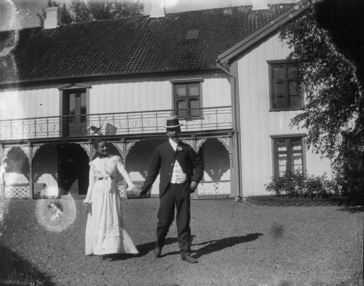 Fredrik Emil Faye, Dobbeltportrett, Selma Faye og Alfred Zimmer som forlovet på Dal, 1900. Paret poserer foran hovedbygningen. Fra portrettserie av personer som bodde på eller besøkte Dal gård, Ullensaker, fotografert av gårdens eier, kammerherre Fredrik Emil Faye (1844-1903) i årene 1875-1900.