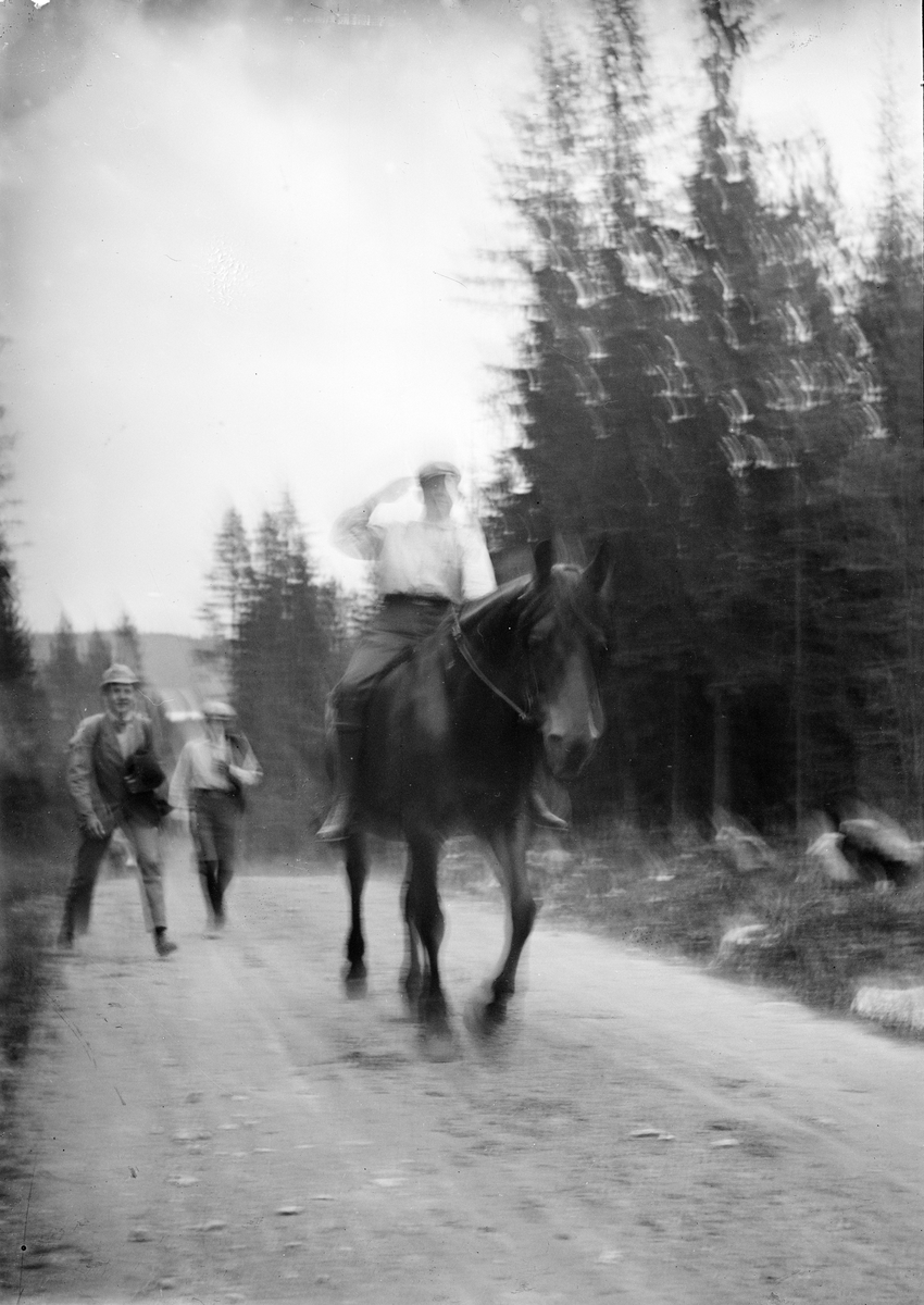 Okänd,, Man rider på häst på skogsväg och två män promenerar efter, sannolikt i Sverige