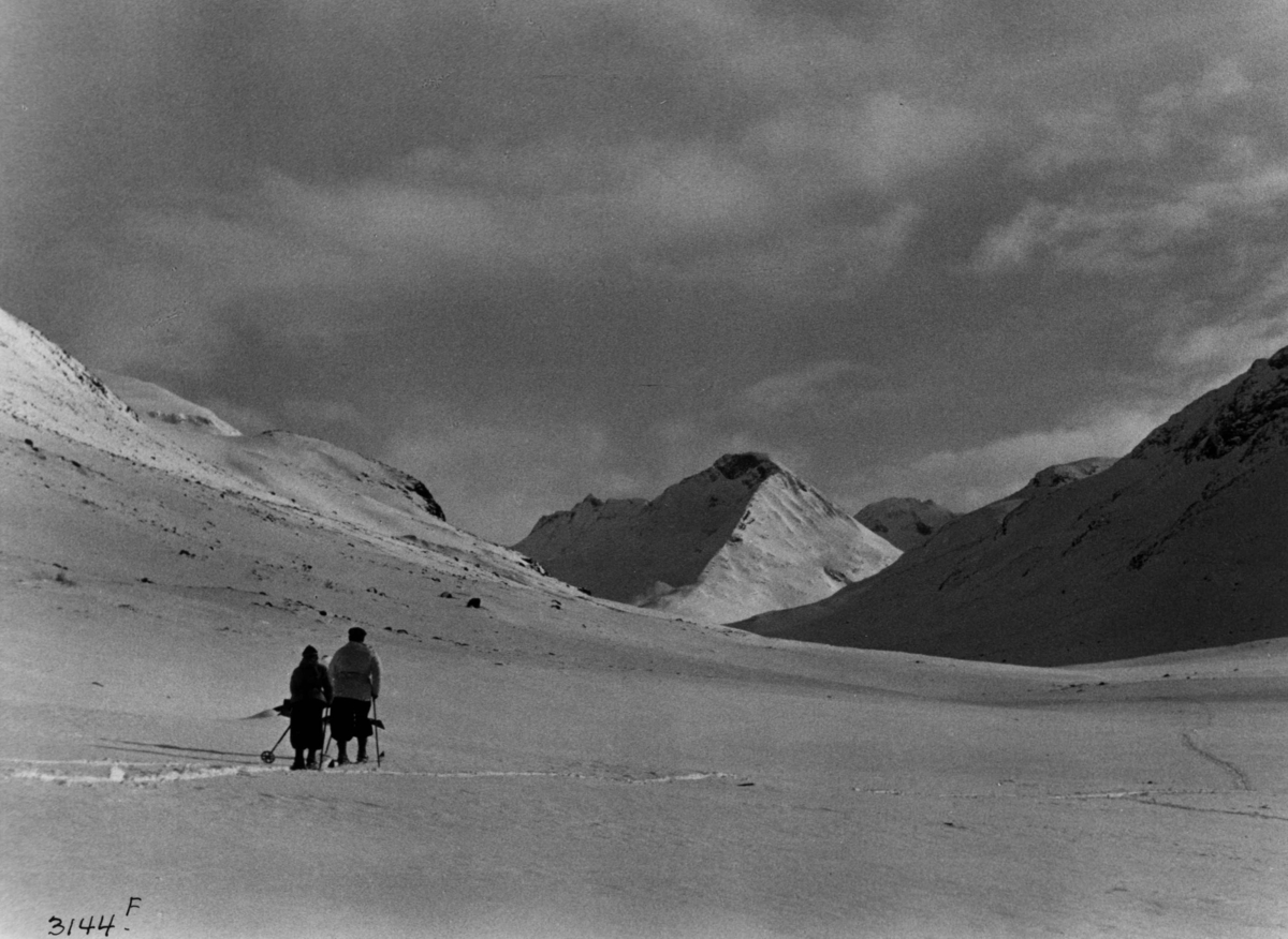Anders Beer Wilse, Skiløpere i Uladalen i Jotunheimen med snødekte fjell og sol.