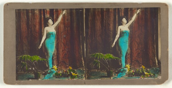 Unknown, [Woman with one arm extended up, looking up, with plants at her feet, with studio backdrop]