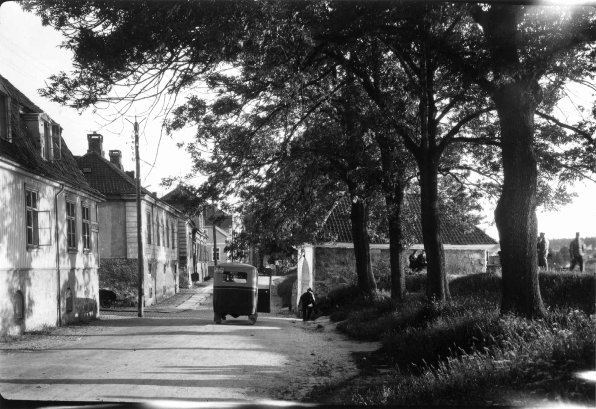 Hermann Christian Neupert, Gatemotiv fra Gamlebyen i Fredrikstad med bil, hus og trær. Folk spaserer på vollen.