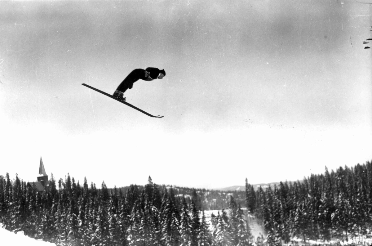 Hermann Christian Neupert, Holmenkollrenn. 1934. Hopper i svevet. Nordmarka og Holmenkollen kapell ses i bakgrunnen.