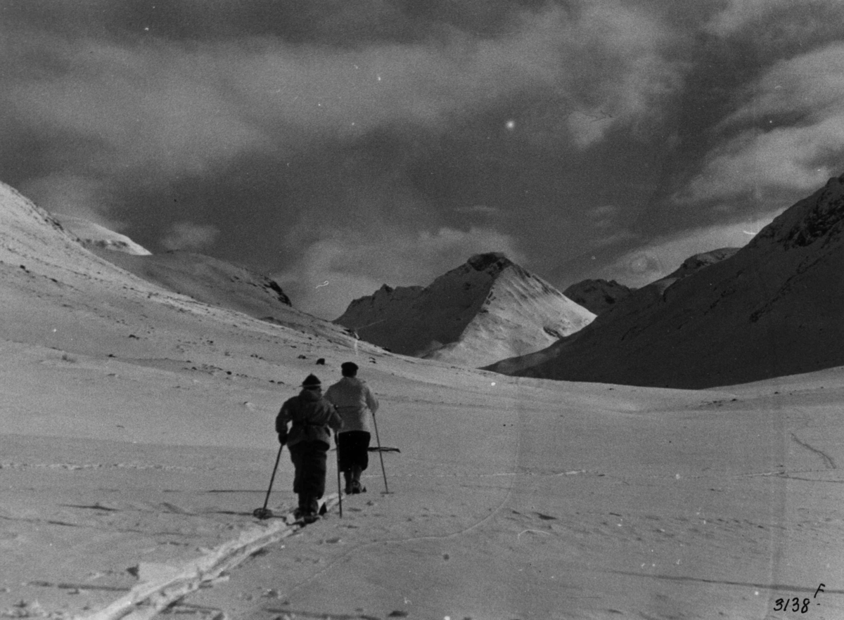 Anders Beer Wilse, Skiløpere i Uladalen i Jotunheimen med snødekte fjell og sol.