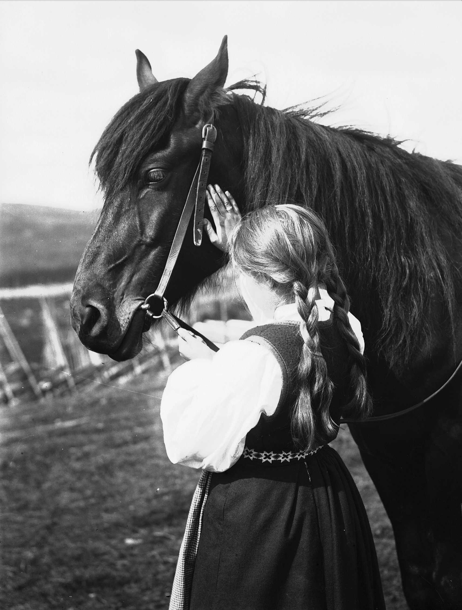 Solveig Lund, Jente i nasjonaldrakt holder i tømmene til en hest og klapper den på nakken. Gjerde i bakgrunnen.