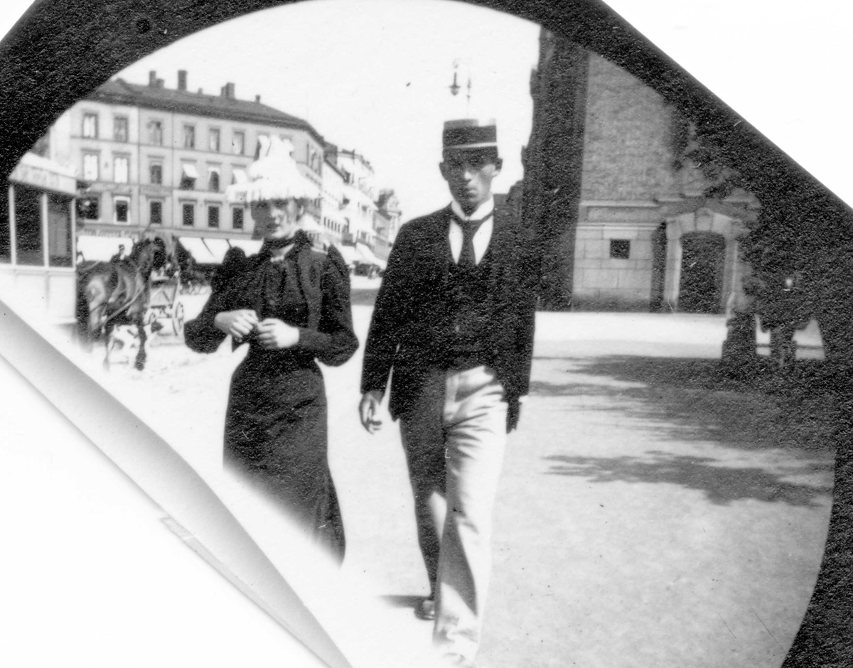 Fredrik Carl Mülertz Størmer, Frk Aagot Lund og en mann spaserer langs Karl Johans gate, Oslo. Stortinget og hestetrikk i bakgrunnen.