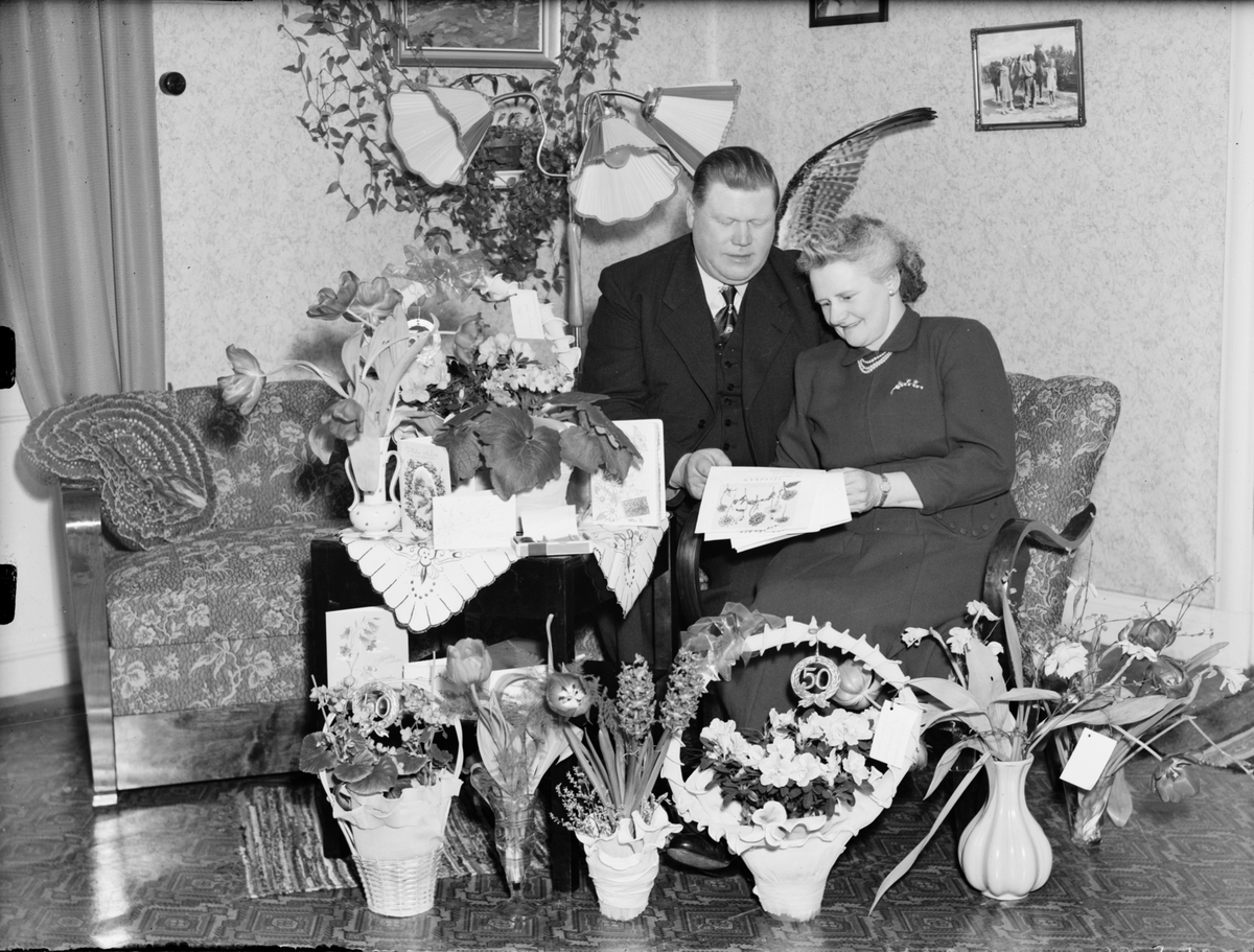 Skötsner-Edhlund, Kvinna och man i hemmiljö omgiven av blommor, Östhammar, Uppland,