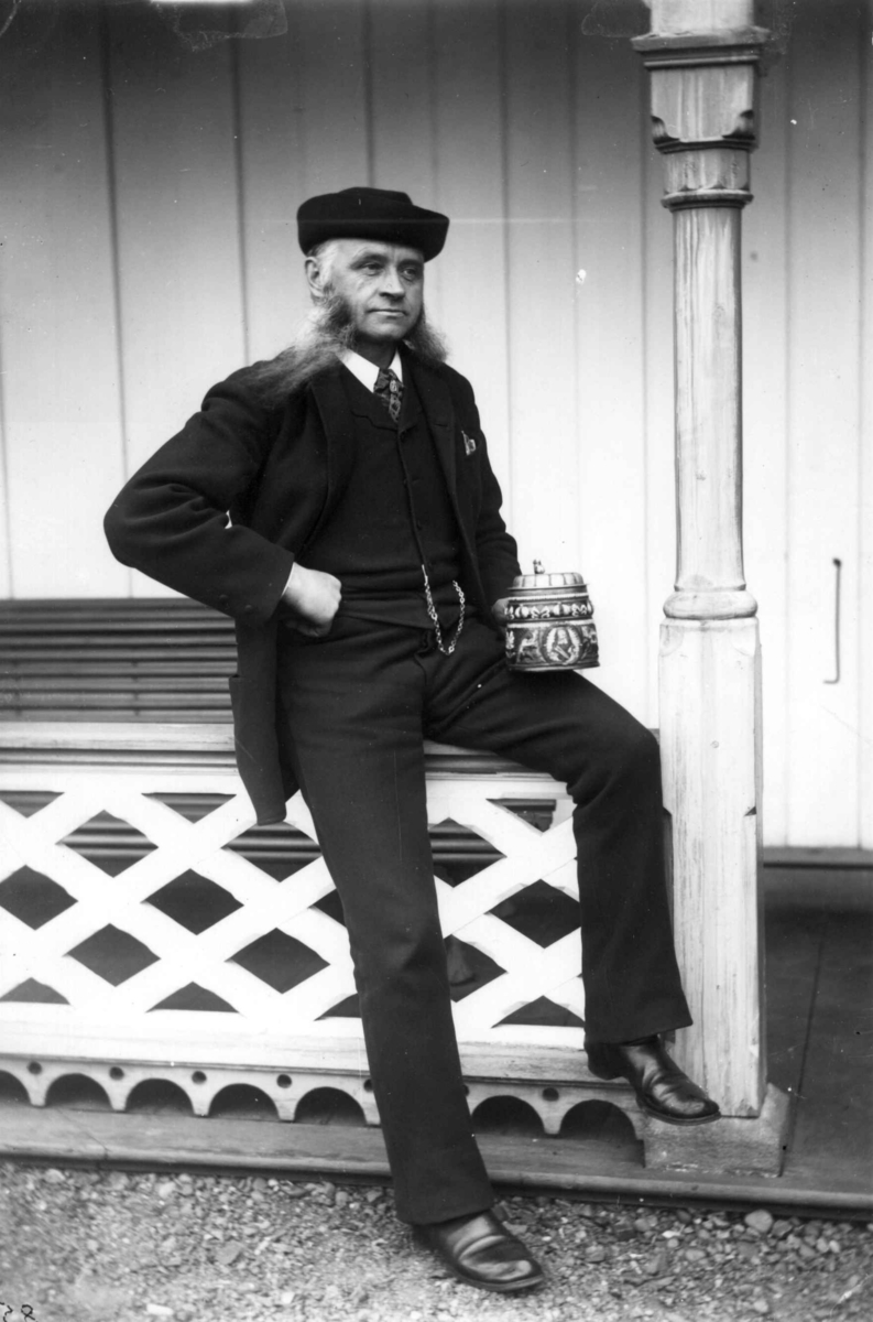 Fredrik Emil Faye, Portrett, Peter Simonsen (1831-95), sittende utendørs på utskåret rekkverk med søyle med et krus (?) i hånden. Fra portrettserie av personer som bodde på eller besøkte Dal gd., Ullensaker, fotografert av gårdens eier, kammerherre Fred. Emil Faye (1844-1903) i årene 1875-1900.