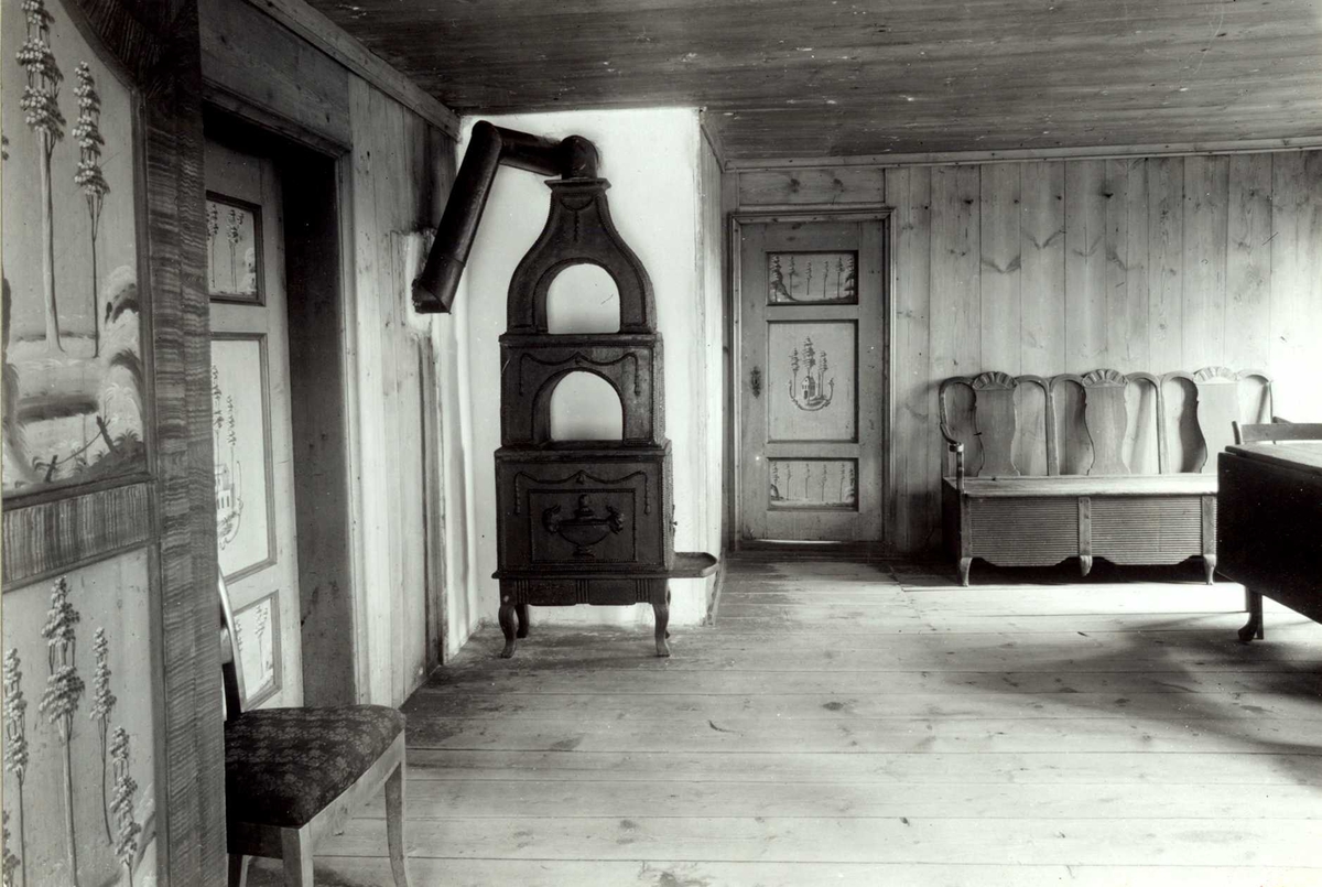 Gisle Midttun, Elisabethstua, Nedre Skjefstad, Elverum, Sør-Østerdal, Hedmark. Interiør med etasjeovn, dekorerte dører, stol, bord og benk. Nå på Glomdalsmuseet.