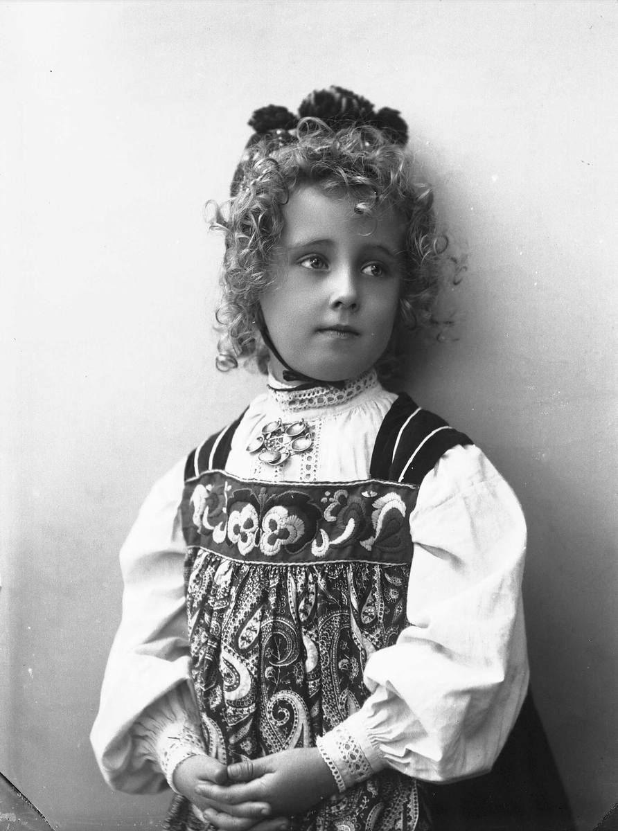 Solveig Lund, Studioportrett av pike i drakt og lue, som holder hendene foldet over magen.