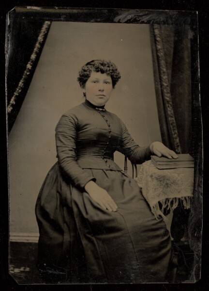 Unknown, [Unidentified woman seated, hand on book on a small table]
