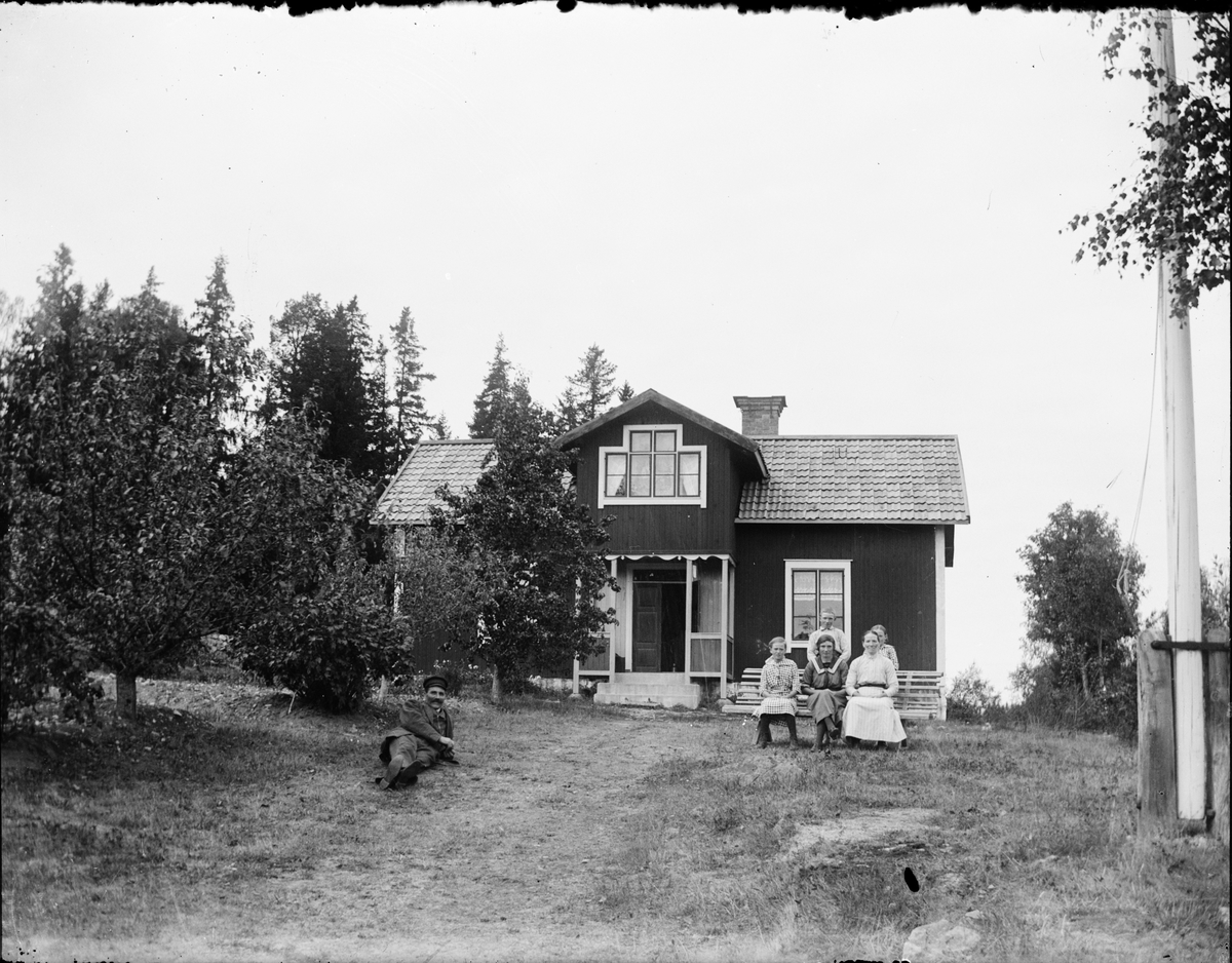 Skötsner-Edhlund, Man liggande i gräset, barn och kvinnor sitter på bänken, framför bostadshus, Östhammar, Uppland