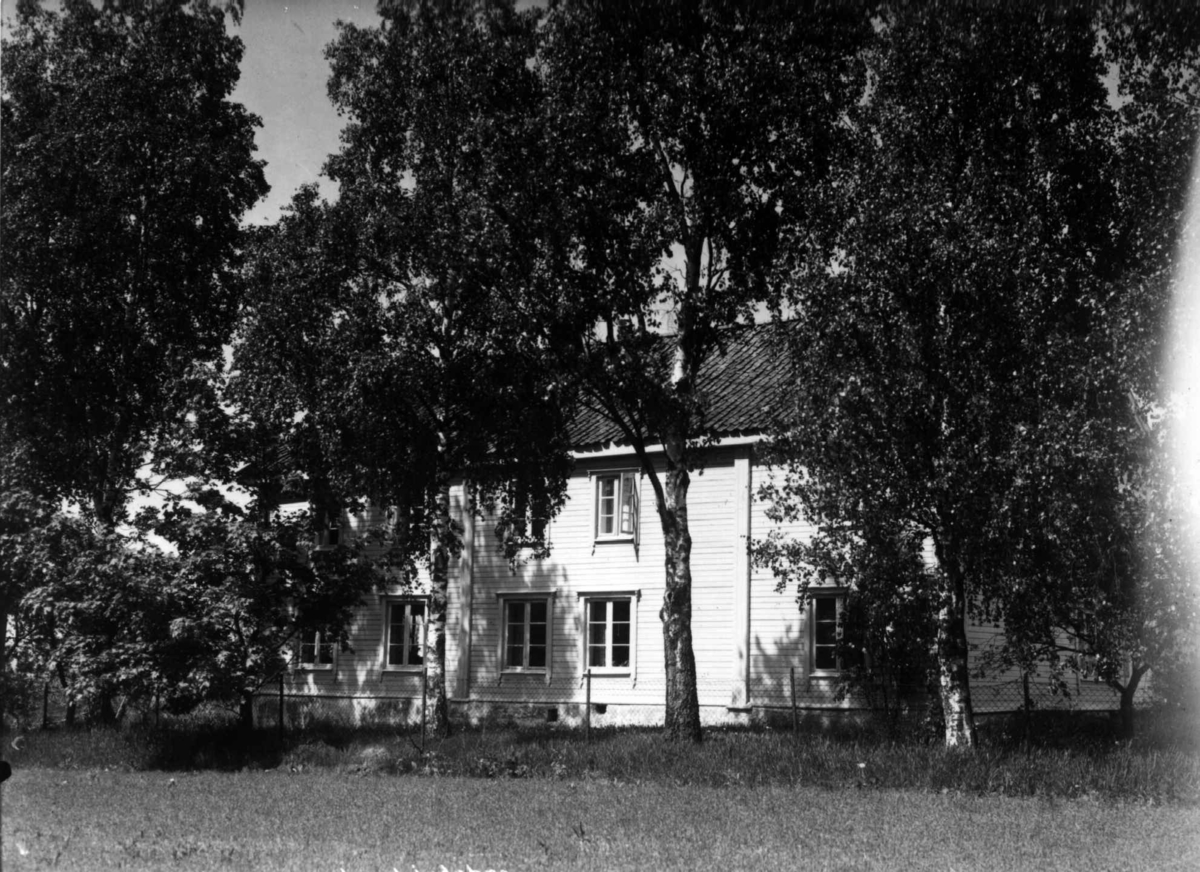 Anders Beer Wilse, Nordre Lindeberg gård, Oslo, Østre Aker. Våningshuset bak trær, fotografert fra et jorde.