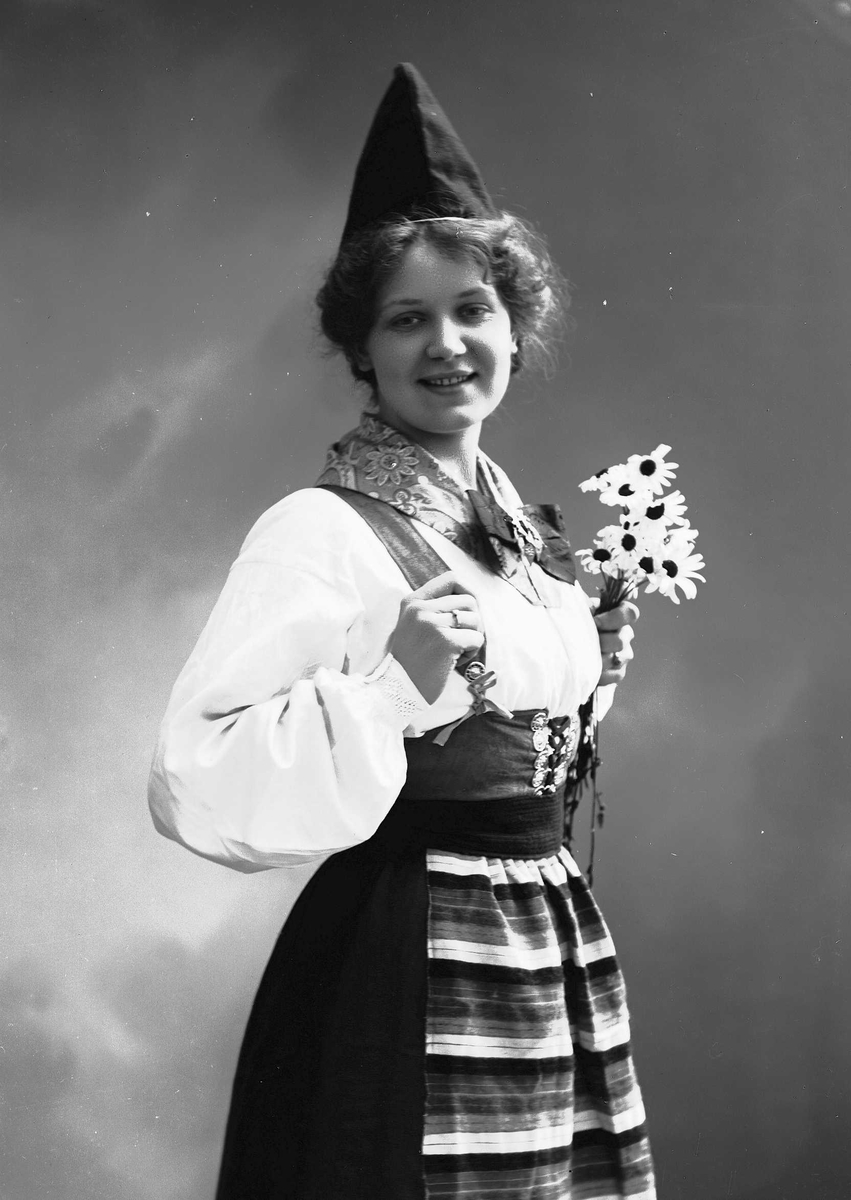 Solveig Lund, Kvinne i drakt og lue, som holder blomsterbukett.