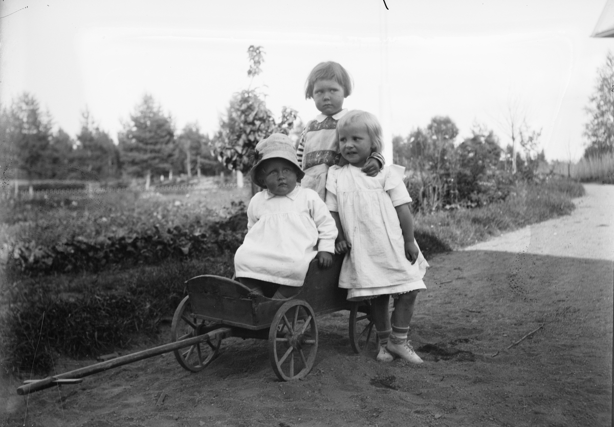 Okänd,, Marit Liljefors och två andra flickor med en liten kärra i trädgård, sannolikt i Sverige