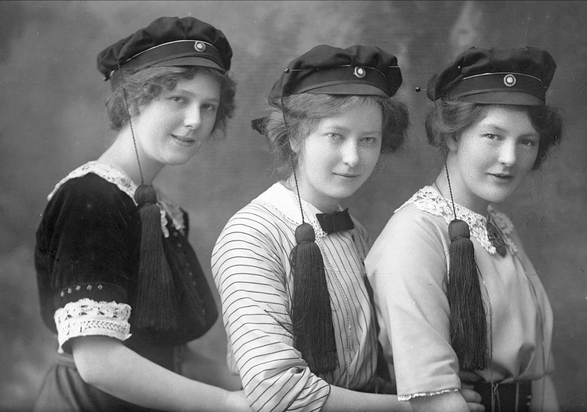 Gustav Borgen, Gruppeportrett, kvinner i studenterluer, søstrene Magnhild (1888-1978), Ingrid (1891-1980) og Gudrun Tøsti (1897-1980). Magnhild var lektor og gift med Ingvar Lillesund, Gudrun og Ingrid var tannleger og drev sin praksis sammen i Oscars gate 92, Oslo. De var ugifte. Søstrene var døtre av statkonsul…