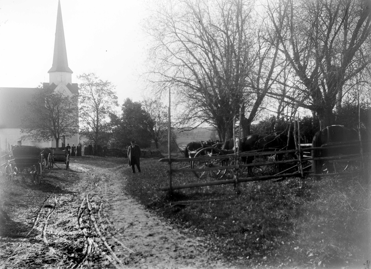 Juliane Fredrikke Langberg, Rakkestad kirke, kirketid med hestetriller stilt utenfor. Gjerde i forgrunnen t.h.. Personer utenfor kirken. Fra malerinne Juliane Fredrikke Langbergs (1856-1930) samling, tatt ca.1895-1910 med motivkrets slekt og venner samt steder tilknyttet samvær med disse.