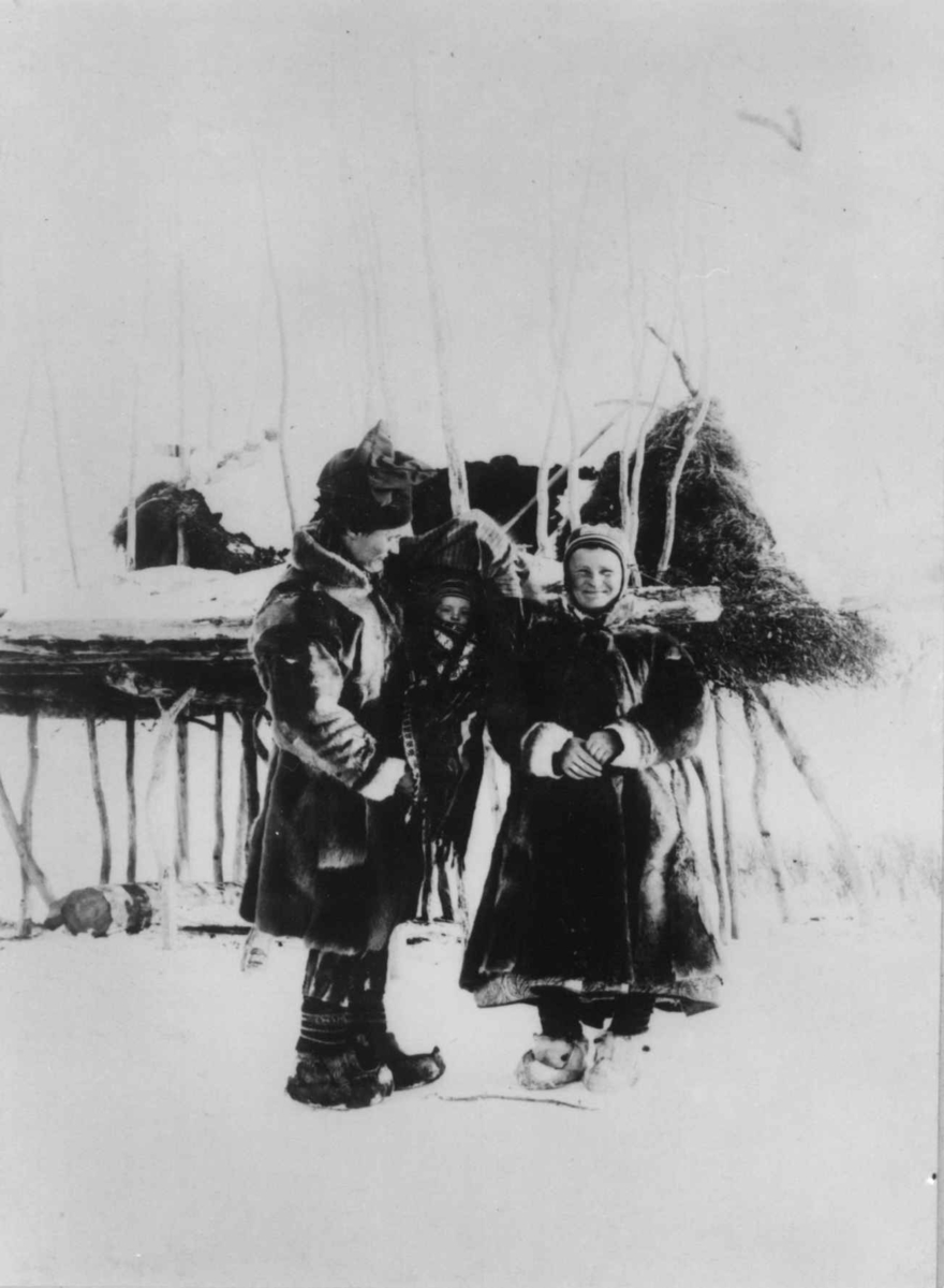 Ellisif Rannveig Wessel, Mann og kvinne med et barn i komse, Ole og Marit Banne med datteren Inga,ved stillas?, Sør-Varanger, Finnmark, ca. 1900.