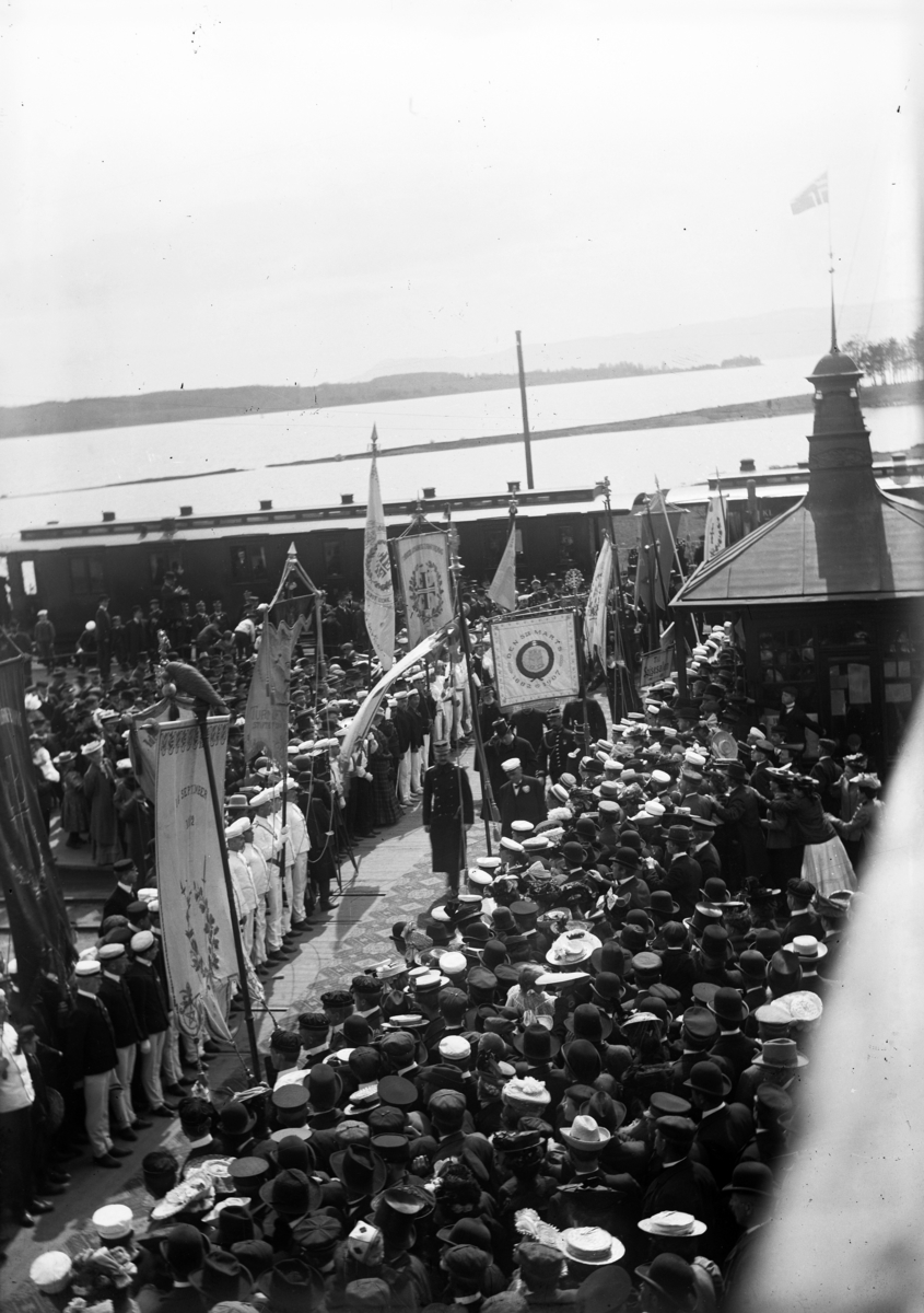 Johannes Larsen Alhaug, Kong Haakon ankommer Hamar jernbanestasjon under det 6. nasjonale landsturnstevnet i 1907. Stor folkemengde.