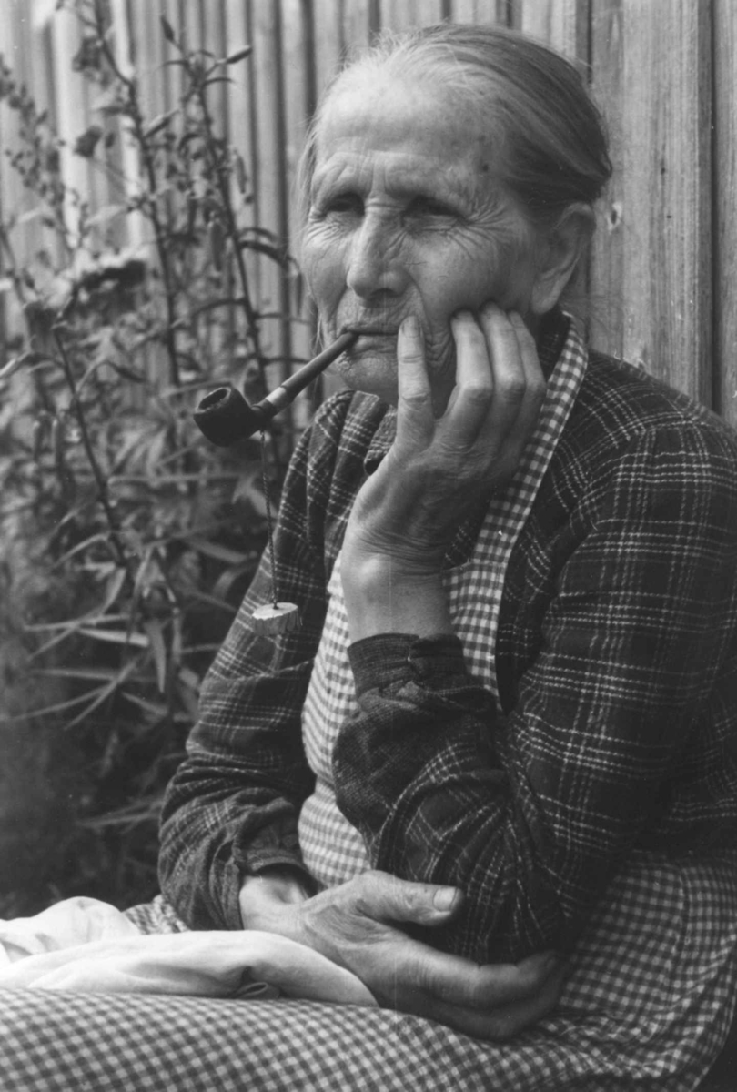 Anna Grostøl, Portrett av en kvinne som sitter og røker pipe. Åseral, Vest-Agder 1943.