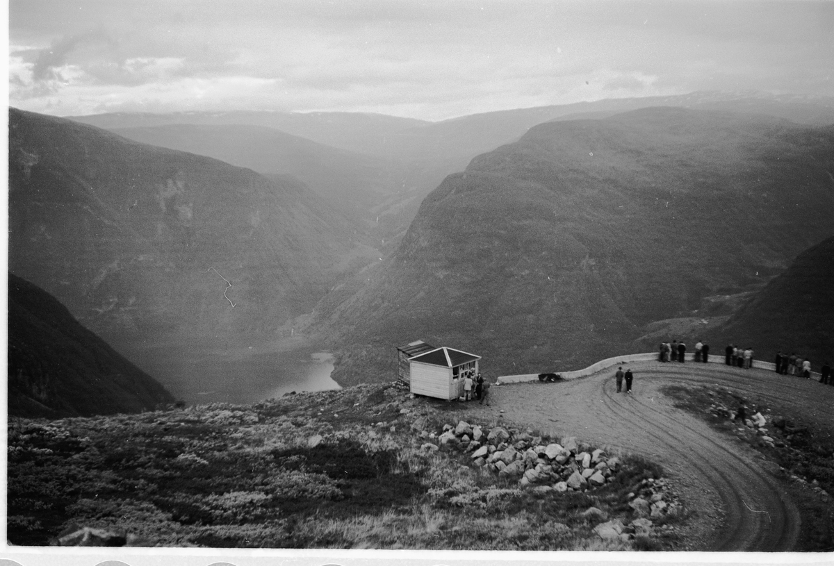 Håkon Prestkværn, VEGEN NED TIL ØVRE ÅRDAL i Sogn og Fjordane. En gruppe mennesker ved en suvenirbutikk.