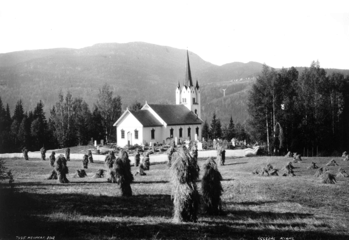 Hermann Christian Neupert, Eggedal kirke, Sigdal, Buskerud. 1930. Landskap. Kornstaurer og gravsteiner. Skog og fjell i bakgrunnen.