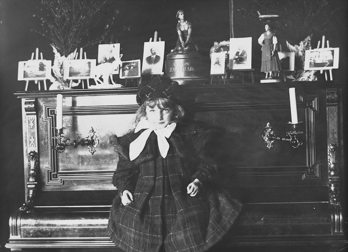 Axel Quinsgaard Wiborg, Karen Q. Wiborg sitter på pianolokk, Meltzers gate 9, Oslo, 1899. Fotografier i ramme plassert på pianoet.