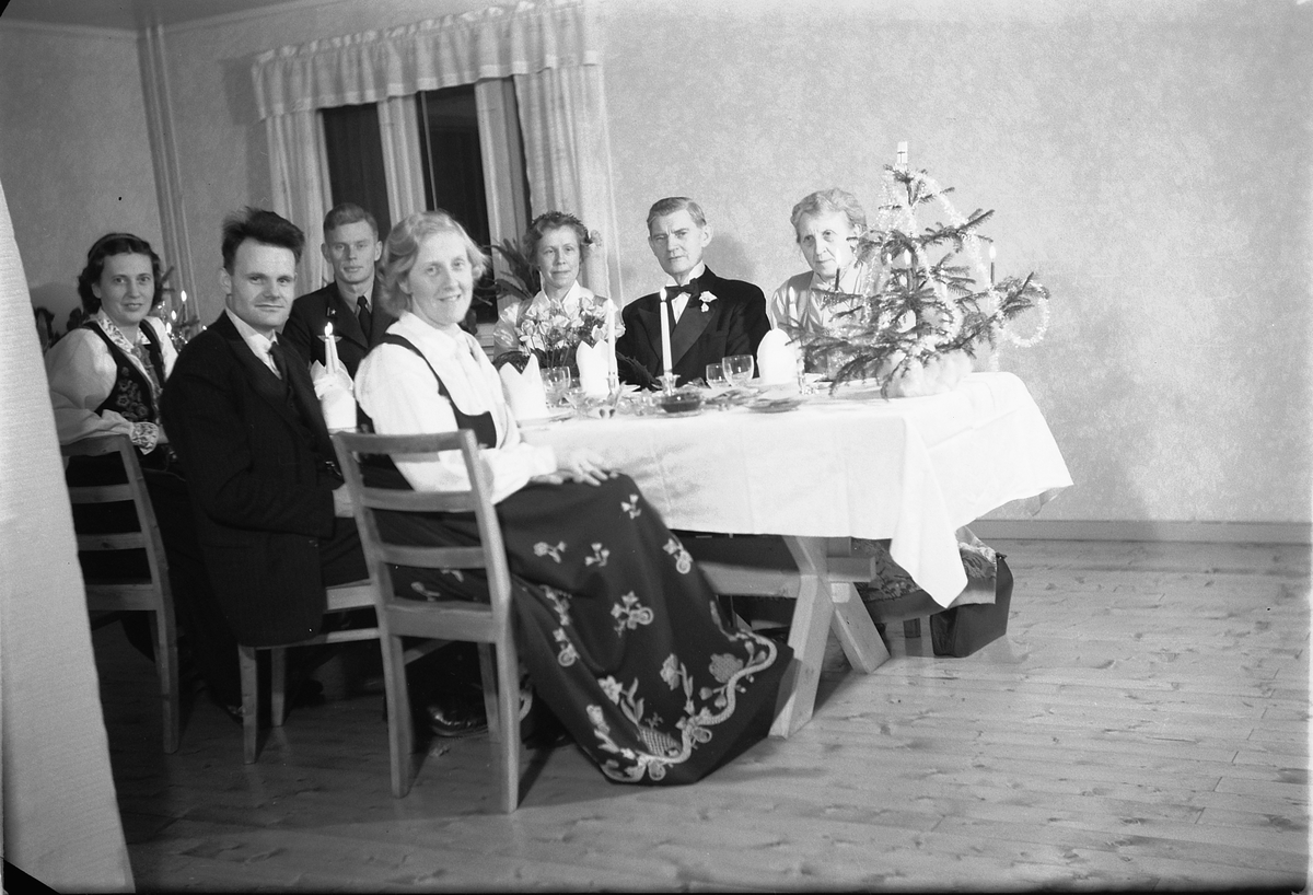 Håkon Prestkværn, Interiør, stue. Ukjent gruppe mennesker rundt et bord med kvinner i bunad.