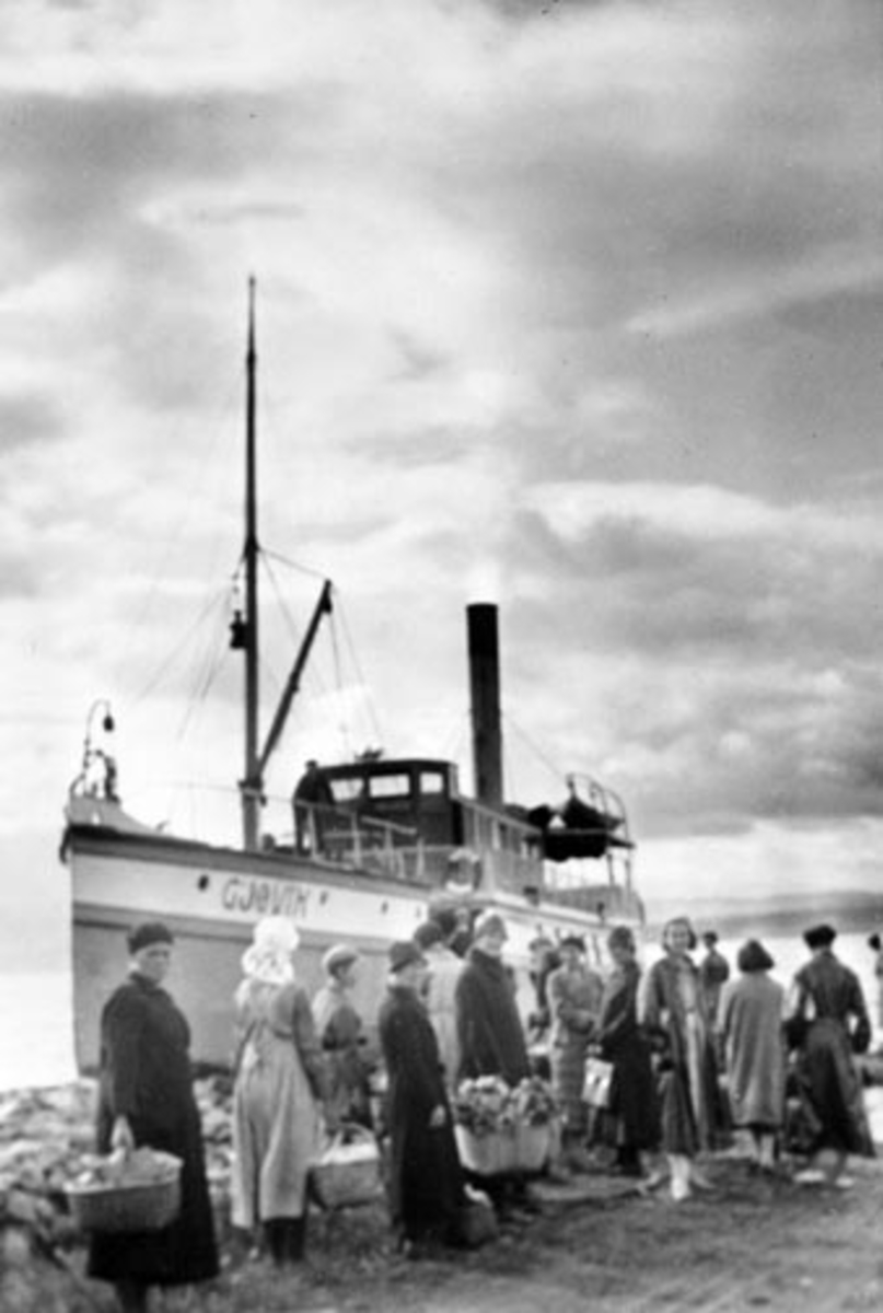 Anno Domkirkeodden, D.S. Gjøvik ved Kisebrygga, Nes, Hedmark.Mye folk. Torvkoner med varer. Fra venstre er Marie Fløttum, Martha Lundstein, Anne Enebakk, Anna Lundstein, Klara Sollien (med ryggen til), Anna Hamborg, Anna Olstad, tre Oslojenter som var på ferie, Arne Hambord og Dorte Hamborg.