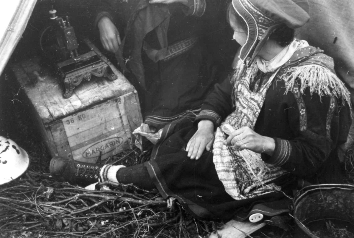 Anna Grostøl, To kvinner ved en teltåpning holder på med skinnarbeid, En symaskin står på en kasse. Olderdalen, Kåfjord, Troms 1947.