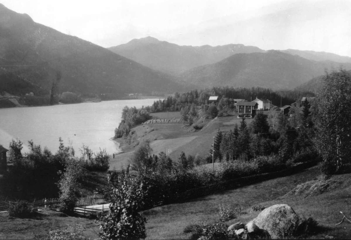 Hermann Christian Neupert, Kravik, Nore, Nore og Uvdal. 1930. Oversiktsbilde. Utsikt mot gården omgitt av jorder og skog. Vann. Fjell i bakgrunnen.