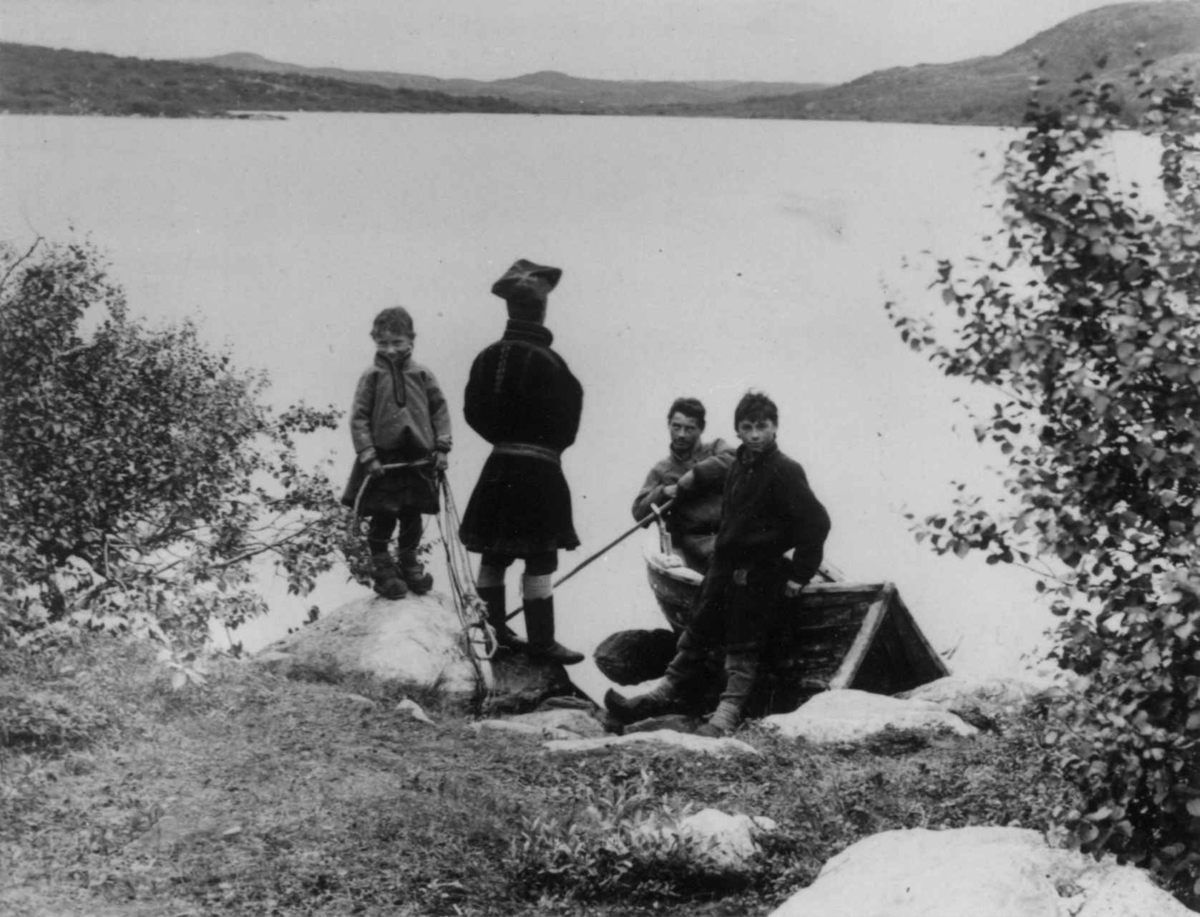 Ellisif Rannveig Wessel, Fire samer ved en robåt i strandkanten, Sør-Varanger, Finnmark, ca. 1900. Gutt med fiskegarn?