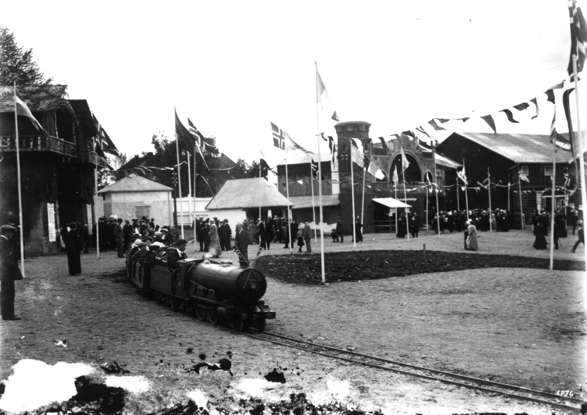 Hermann Christian Neupert, Jubileumsutstillingen på Frogner, Oslo, 1914. Lilleputtbane. Publikum. Paviljonger og flagg i bakgrunen.